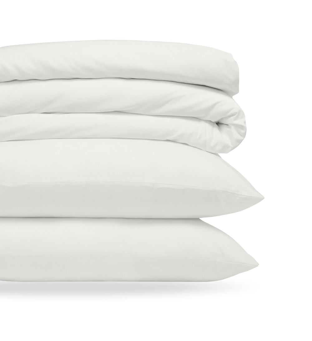 Ensemble de literie blanche pliée avec oreillers et couette, soigneusement disposé pour illustrer douceur et propreté.